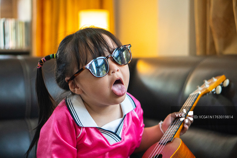 快乐的亚洲儿童戴着太阳镜在家弹吉他唱歌。图片素材
