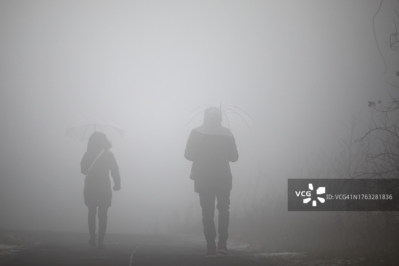 在雾天里，拿着透明雨伞行走的两人图片素材