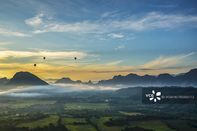 日出时分乡村地区、热气球和山脉的景观图片素材
