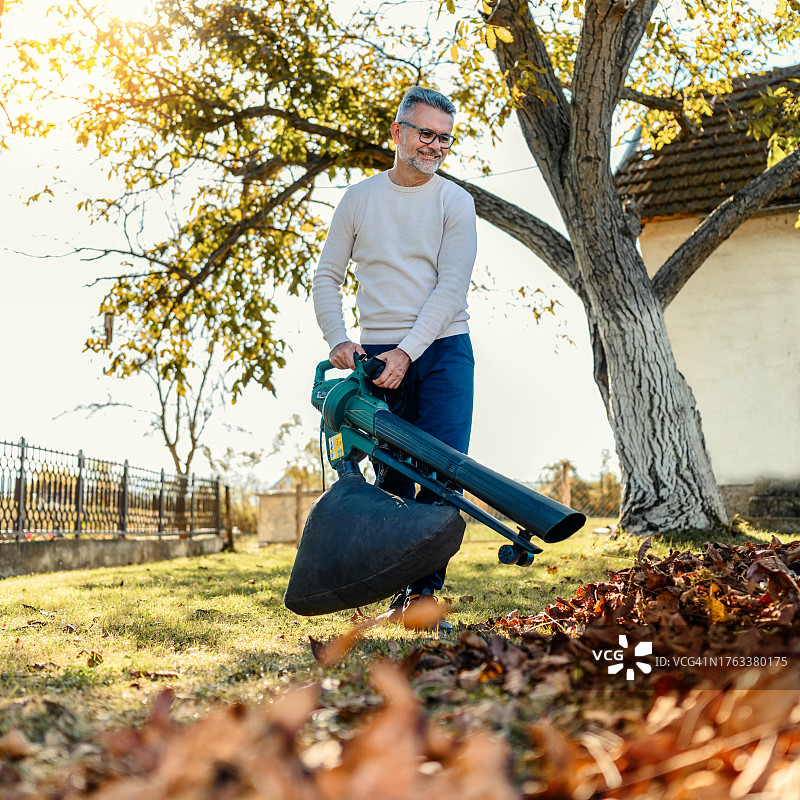 在院子里使用吹叶机的中年男人图片素材