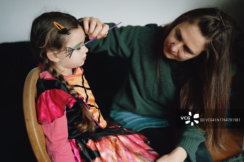 小女孩打扮成女巫坐在椅子上，妈妈给她画脸图片素材