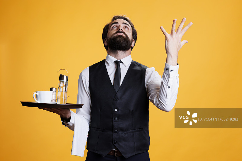 拿着托盘在黄色背景前做手势的神秘服务员肖像图片素材