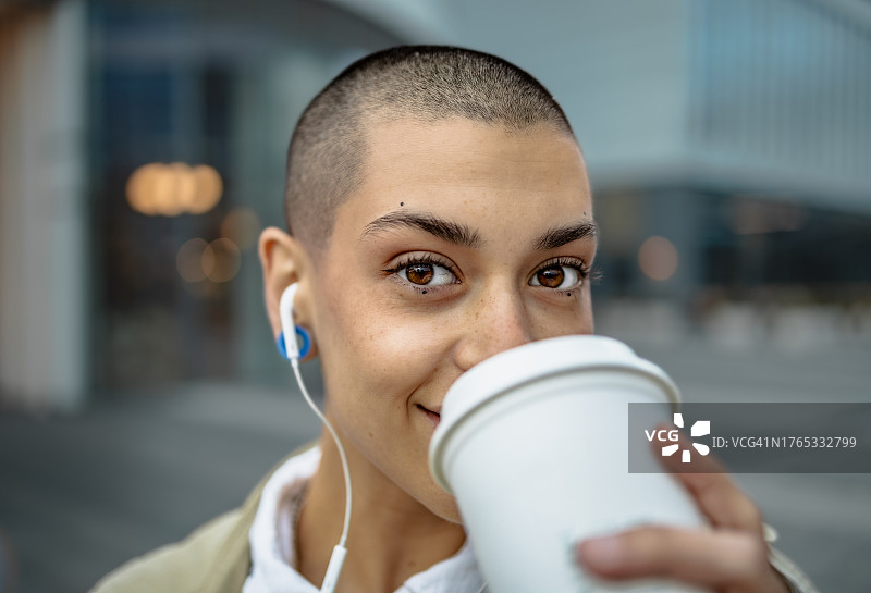 在现代建筑旁用手机喝咖啡的年轻女子特写图片素材