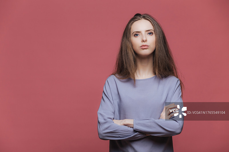 自信迷人的休闲女性特写，双手交叉，严肃地看着镜头，背景为粉红色图片素材
