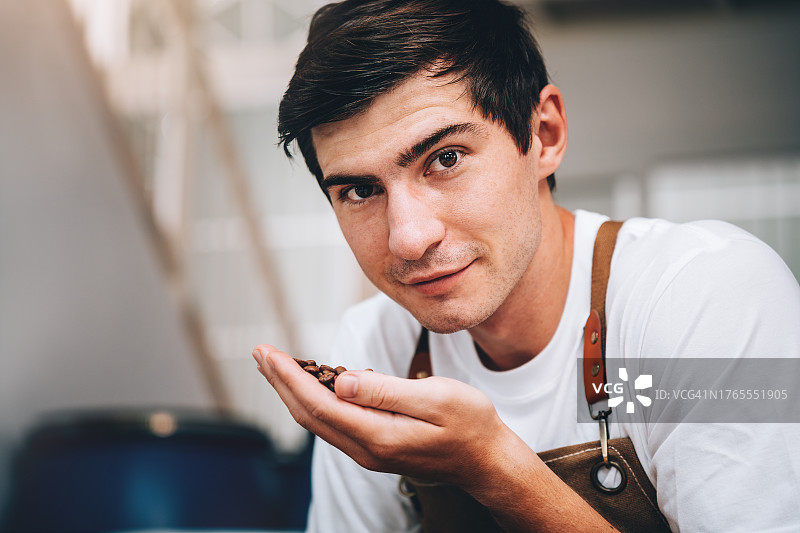 年轻男子手持烤咖啡豆检查质量的肖像图片素材