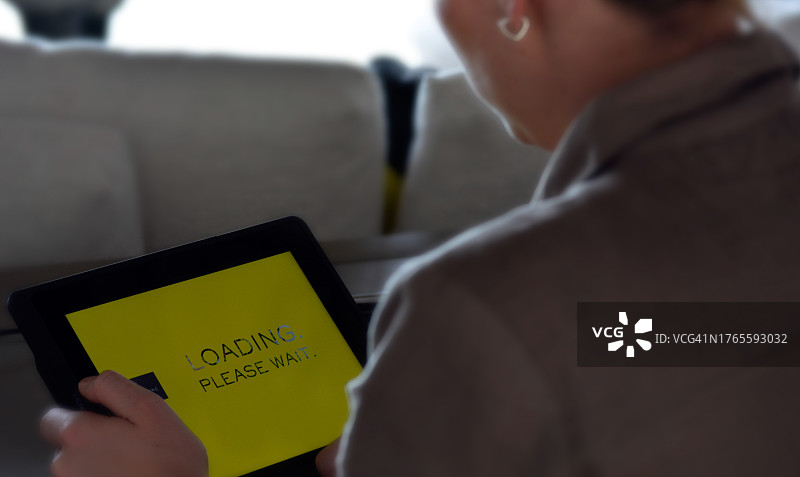 女人在家中使用平板电脑，屏幕为黄色，显示“加载”字样。特写图片素材