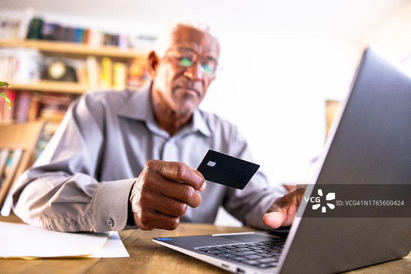 年长黑人男人用信用卡在笔记本电脑上购物图片素材