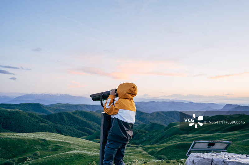 在山顶用双筒望远镜观察的男孩，享受健康童年图片素材