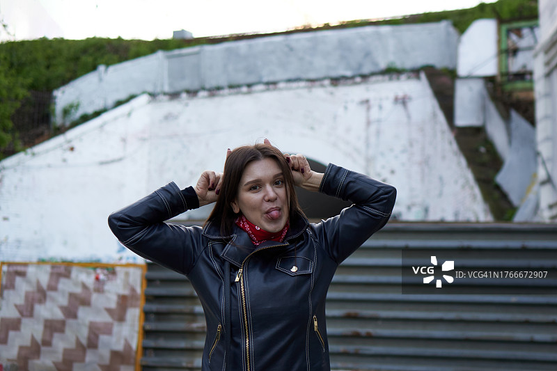 在贫民窟背景下，身穿皮夹克和红色领巾的快乐年轻女子肖像。健康积极的生活方式图片素材