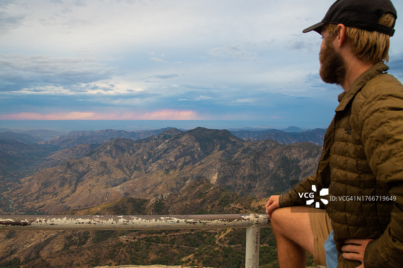 男子站在栏杆旁，眺望远处山谷中的村庄，美国加利福尼亚州红杉国家公园图片素材