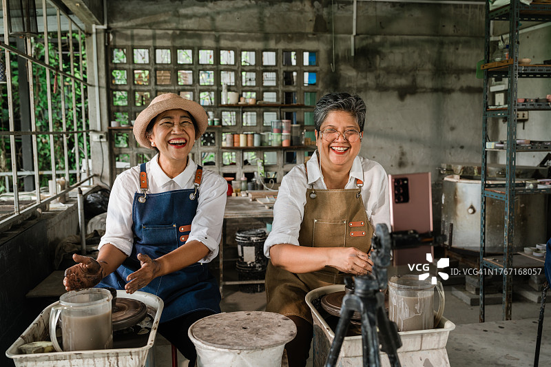 两位年长的女性朋友在智能手机上直播陶艺课，笑容满面图片素材