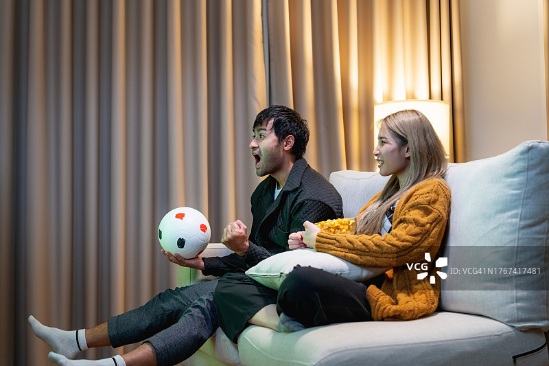 亚洲夫妇在家看电视为足球欢呼图片素材