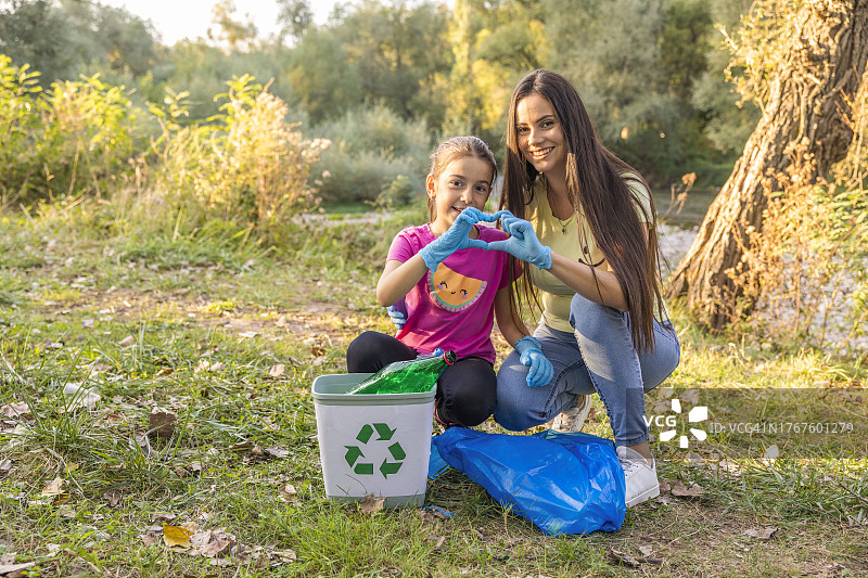 女志愿者与小女孩一起用手指比心，成功收集塑料瓶进行回收图片素材