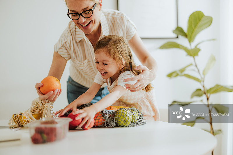 快乐的母亲和女儿一起从网袋里取出食品杂货图片素材