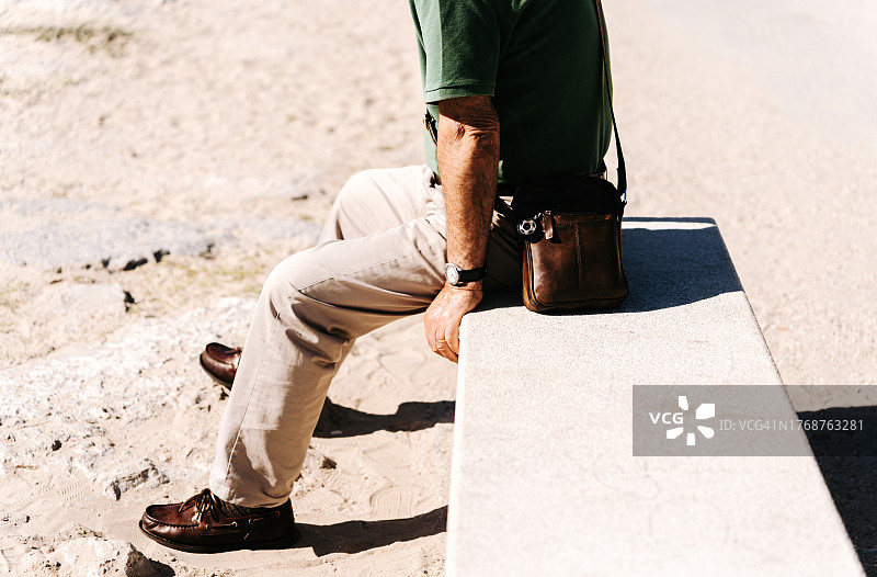身份不明的老人坐在海滩的石凳上图片素材