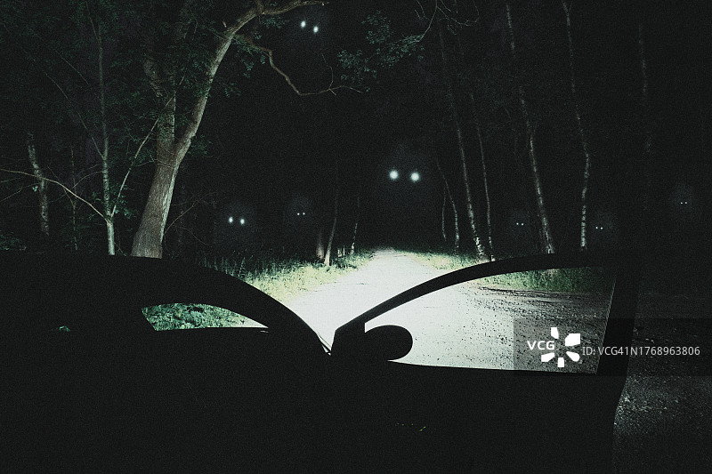 发光眼睛的可爱幽灵在闹鬼的森林里漂浮。夜间有汽车停在路边图片素材