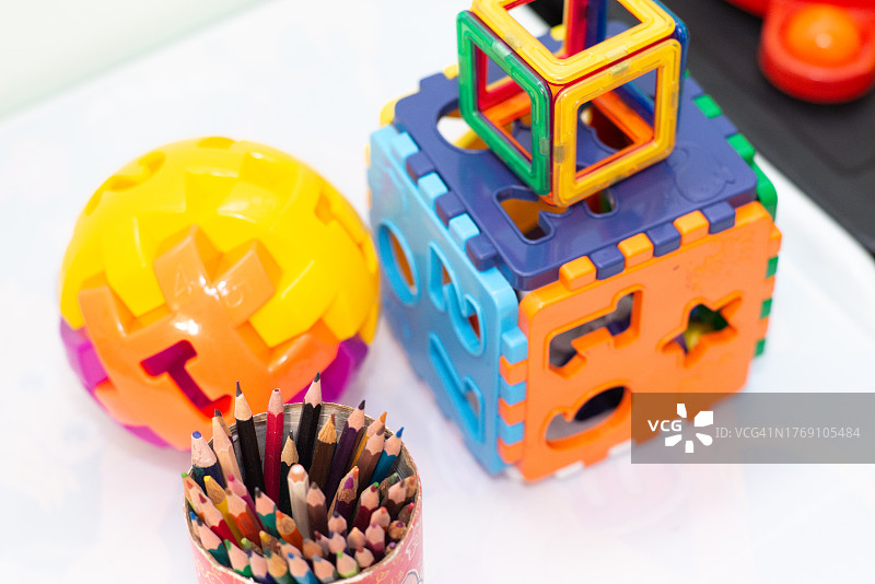 白色桌子上塑料制成的彩色插件玩具和一个装有不同颜色铅笔的罐子图片素材