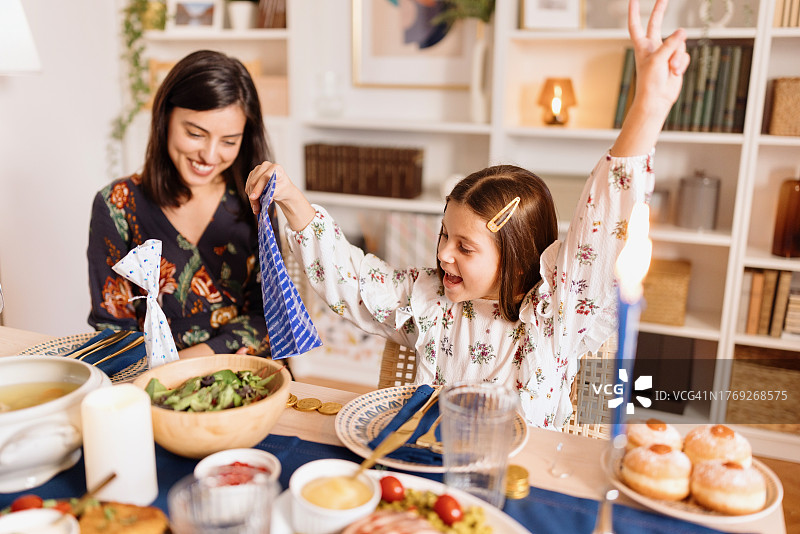 在传统的光明节晚餐上，快乐的小女孩正在打开她的巧克力图片素材