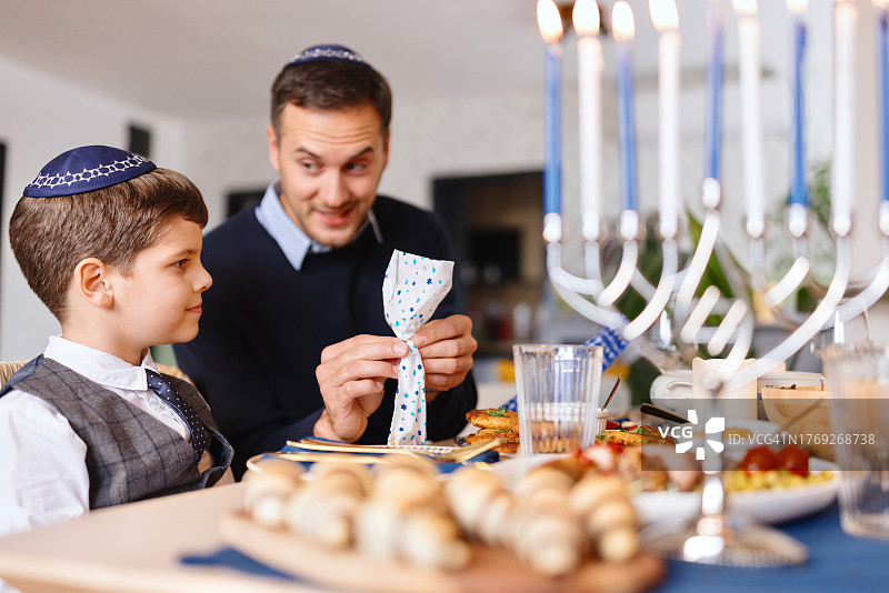 父亲和儿子在传统光明节晚餐上打开礼物特写图片素材