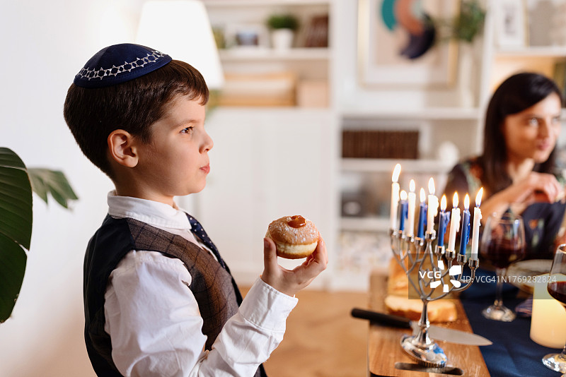 可爱的小男孩在传统光明节晚餐期间吃Sufganiyot图片素材