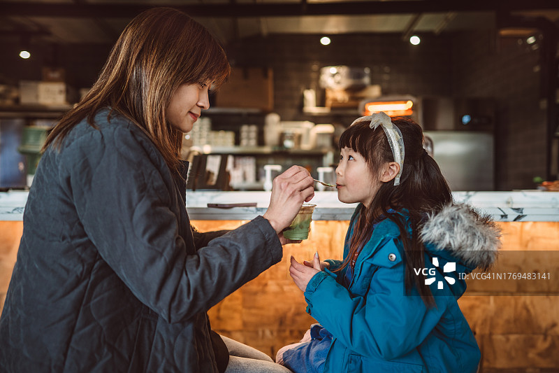 年轻漂亮的亚洲妈妈在咖啡馆里给可爱的女儿喂冰淇淋图片素材