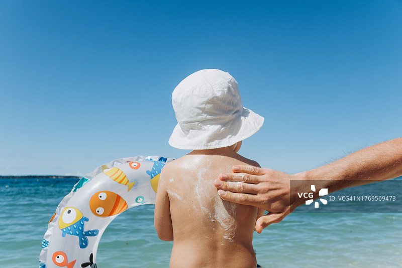 父亲在海滩上为孩子涂抹防晒霜图片素材