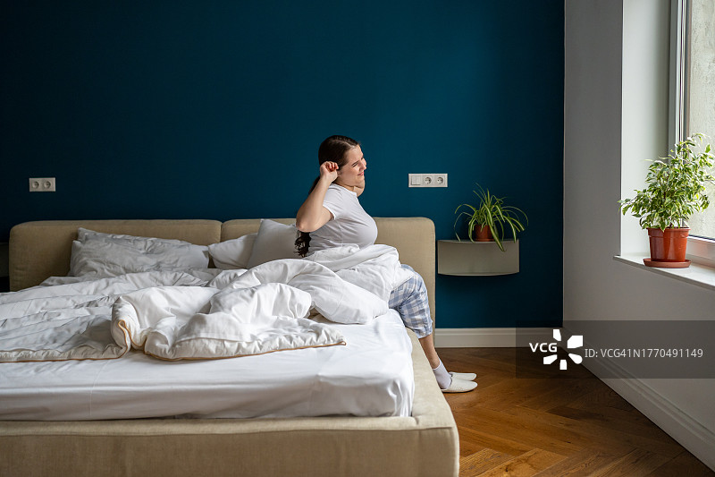 在舒适公寓的床上醒来，感觉良好并伸展微笑的超重女人图片素材