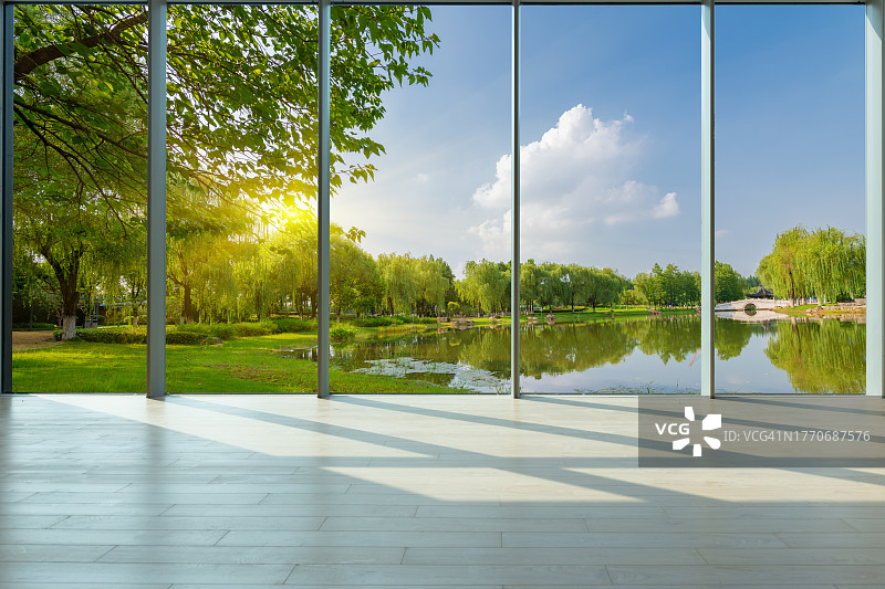 透过玻璃窗看城市公园的池塘、草坪和绿色树林图片素材