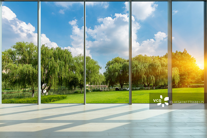 透过玻璃窗，晴空下，城市公园的草坪和绿色森林图片素材