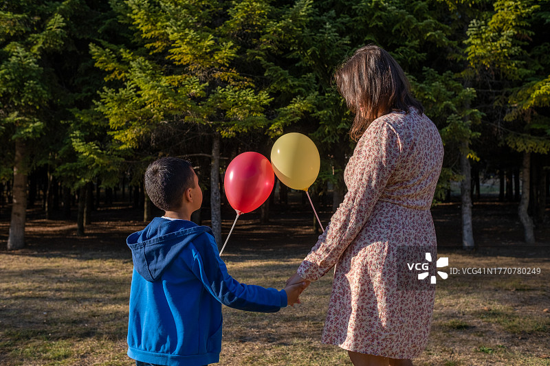 年轻女子和孩子在公园里玩耍，拿着两个气球图片素材