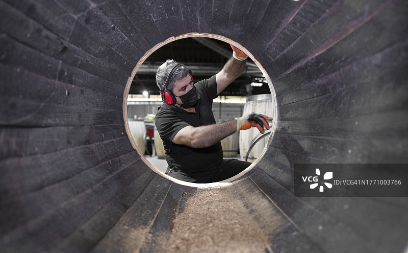 在雪利酒桶厂，一名工人正在密封桶的内部。照片是从桶内部拍摄的图片素材