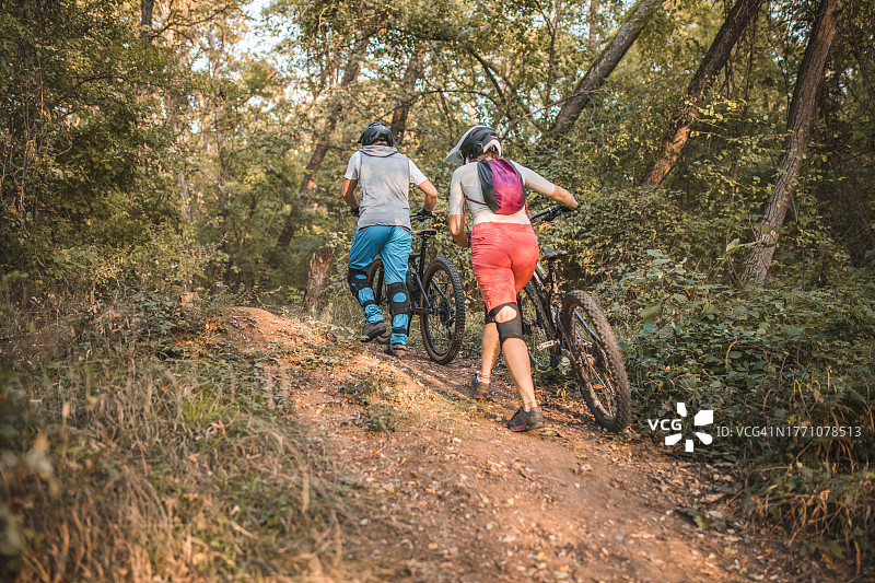 两位朋友推着自行车穿过森林到达下坡点的背影图片素材
