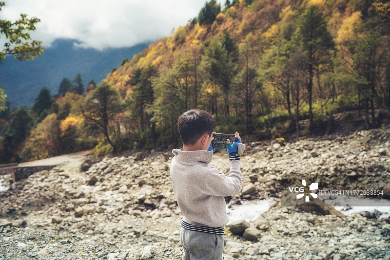 男孩用手机拍摄秋景图片素材