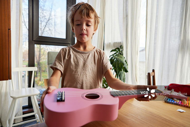 小男孩在家笑着从桌子上拿起尤克里里琴图片素材