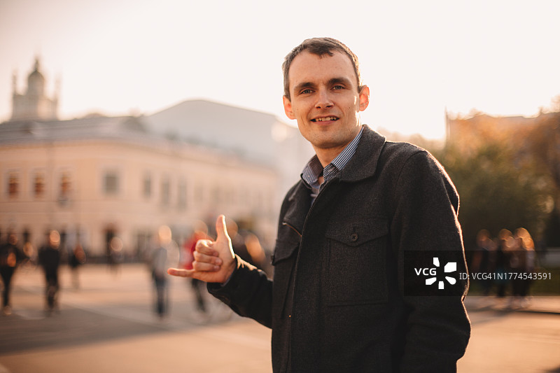 快乐的年轻男子在城市街道上做出shaka手势图片素材