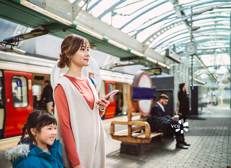 年轻漂亮的亚洲女子在站台上用手机查看列车信息，与女儿一同旅行图片素材