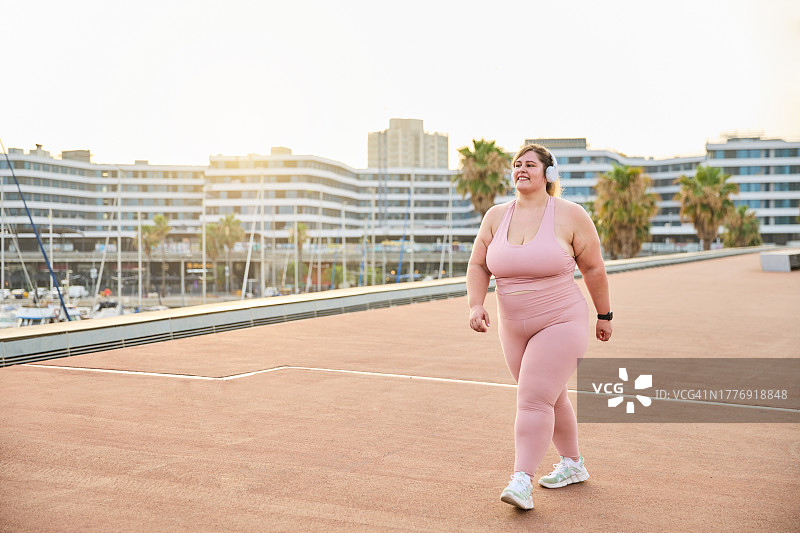 戴着耳机在港口跑步的快乐大码女性图片素材