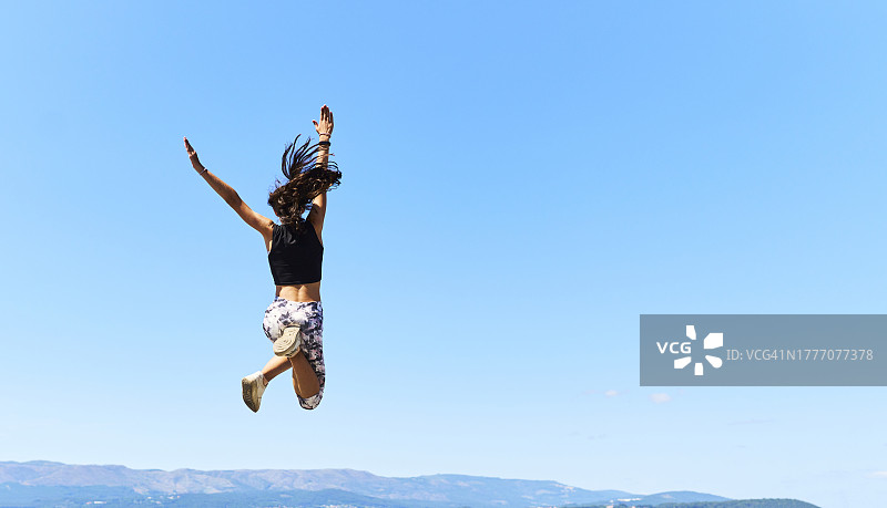 在码头上跳跃的年轻女子后视图，背景是天空图片素材