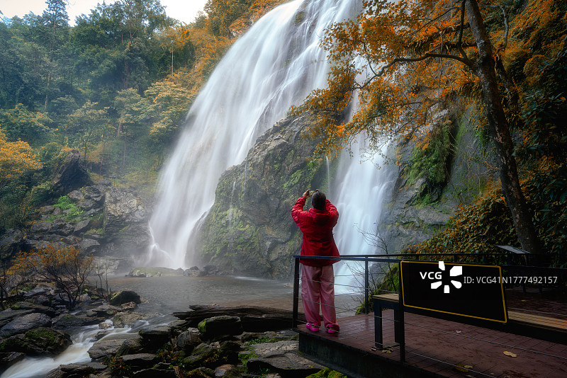 泰国甘烹碧府空朗兰瀑布，年轻女子用手机在壮丽的瀑布前拍照图片素材
