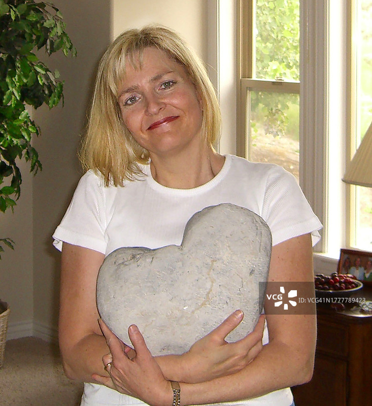 一位美丽的绿色眼睛金发女士拿着一块大的心形石头图片素材