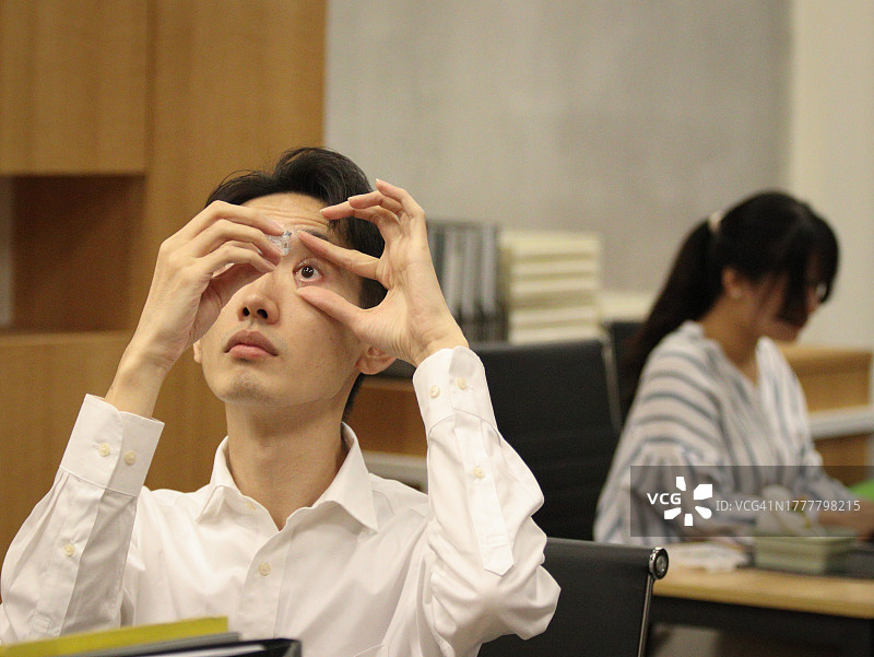 长时间工作后眼睛不适，准备滴眼药水的亚洲男人图片素材