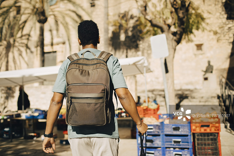 男游客背着背包在阳光明媚的日子里逛市场的背影图片素材