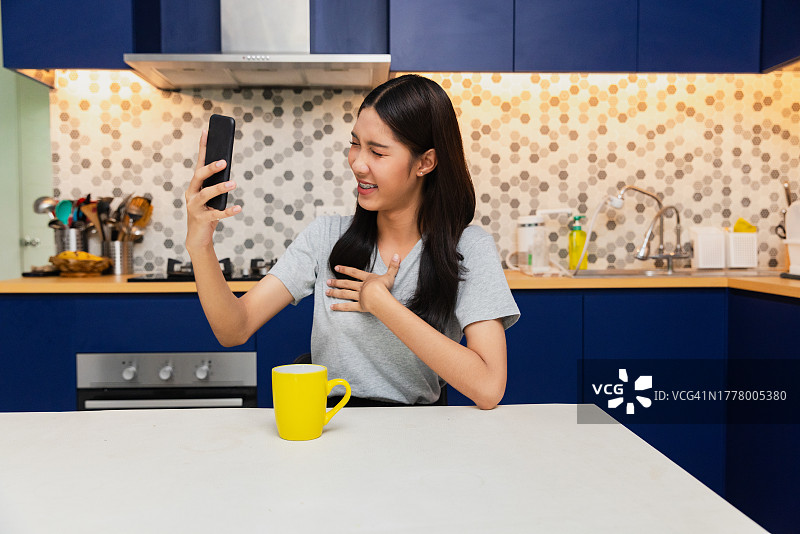 年轻的亚洲女人在厨房里用手机进行视频通话图片素材