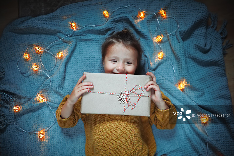 圣诞节环保礼物和灯光氛围：儿童毛衣拿着环保礼品盒，棕色纸条纹丝带和木制雪花，俯视图图片素材