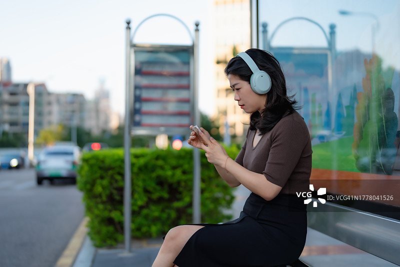 在公交车站用智能手机听音乐的女人图片素材