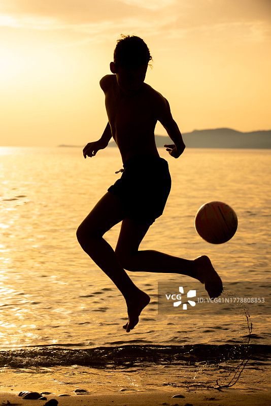 日落时分在海滩上踢足球的男孩剪影图片素材