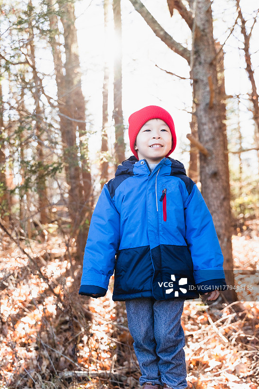 戴着红色无檐小便帽的自信亚洲男孩在森林里拥抱乐趣图片素材