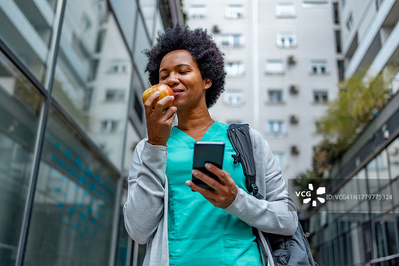 拿着苹果在户外行走的非裔美国女护士图片素材