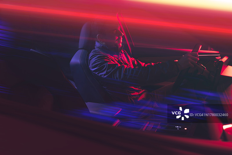 夜晚驾驶汽车，车灯拖着红色尾迹的快乐男人图片素材