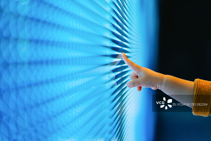 孩子的手触摸发光的LED显示屏的特写。孩子的手指指向黑暗中蓝色的数字显示屏。连接未来。未来主义。创新、生活方式和科技概念图片素材